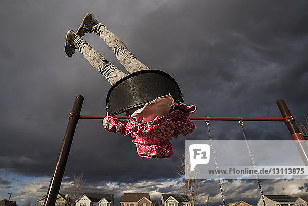 Tiefblick auf ein spielerisches Mädchen  das auf einer Schaukel gegen stürmische Wolken auf dem Spielplatz schaukelt