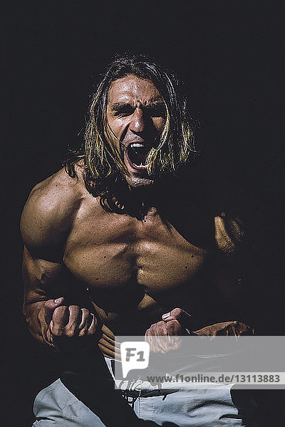 Shirtless man screaming while standing in darkroom at gym