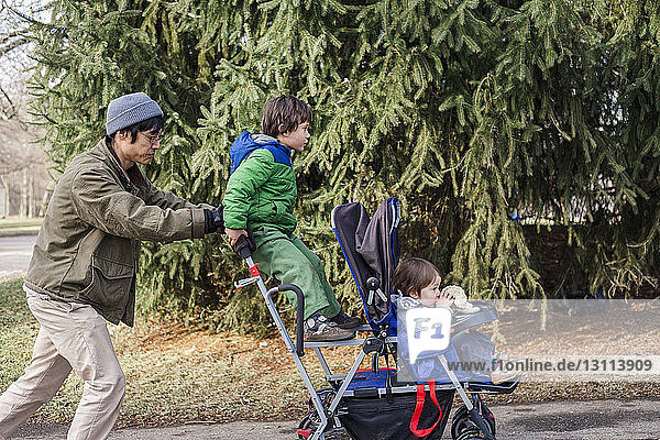 Side view of father pushing children sitting on baby stroller at park