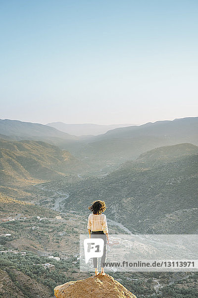 Rückansicht einer Frau  die die Landschaft betrachtet  während sie auf einem Felsen vor klarem Himmel steht