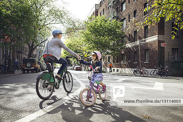 Mother and daughter giving high-five while riding bicycles on street