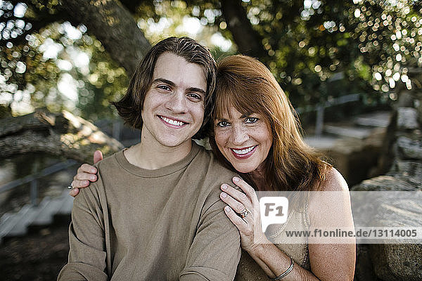 Portrait of happy mother with son sitting against trees at park