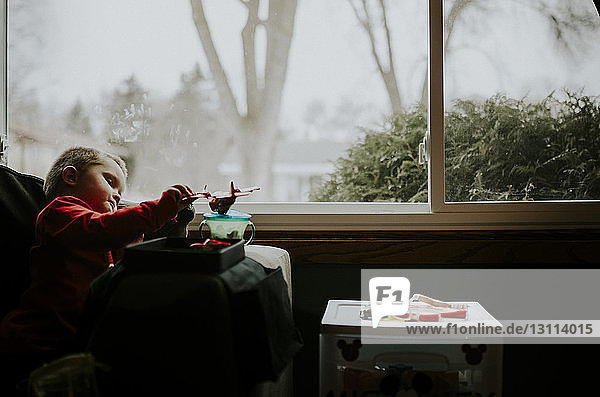 Junge spielt mit Spielzeug  während er zu Hause auf einem Stuhl am Fenster sitzt