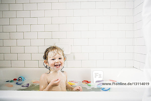 Porträt eines fröhlichen Mädchens  das in einer Badewanne vor einer gefliesten Wand badet