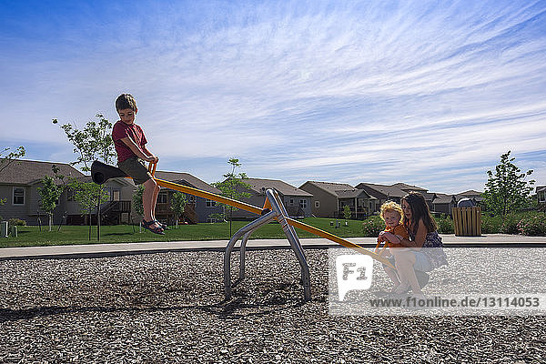 Geschwister spielen am sonnigen Tag im Park auf der Wippe gegen den Himmel