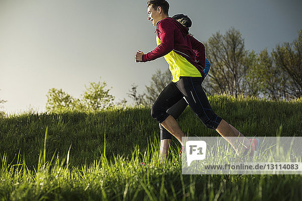 Side view of athletes running on grassy field during sunset