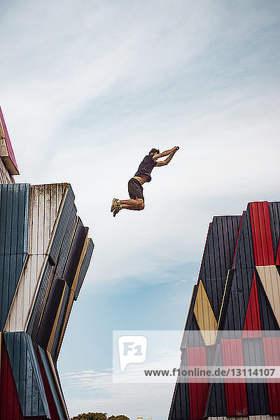 Niedrigwinkelansicht eines Mannes  der über Gebäude gegen den Himmel springt