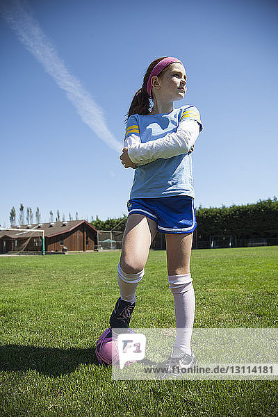 Selbstbewusstes Mädchen mit Fussball auf Grasfeld gegen den Himmel