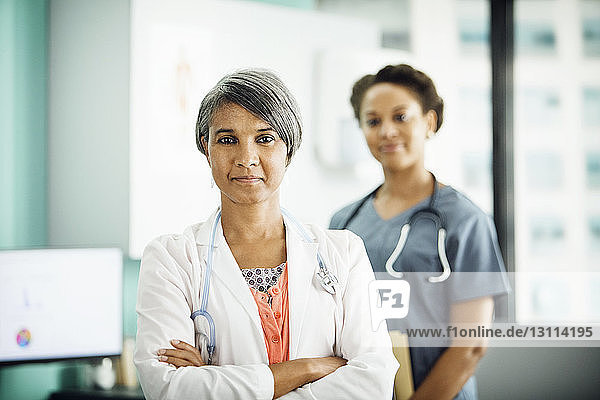 Portrait of confident female doctor standing arms crossed with colleague in background
