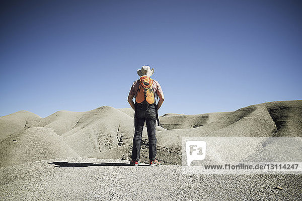 Rear view of male hiker standing at desert against clear blue sky