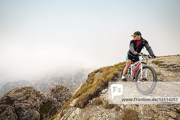 Male athlete with bicycle on mountain against sky