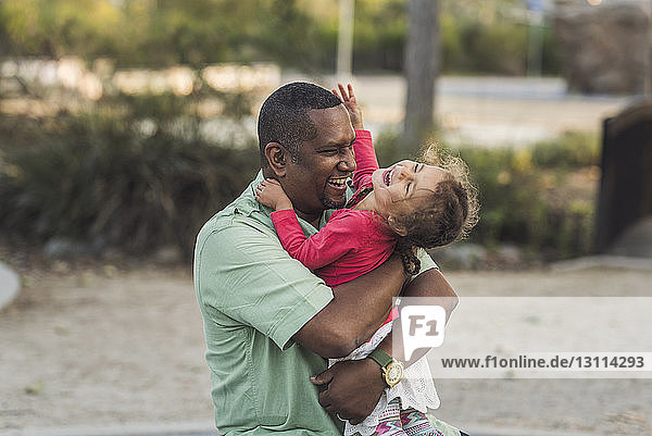 Fröhlicher Vater spielt mit niedlicher Tochter auf dem Spielplatz