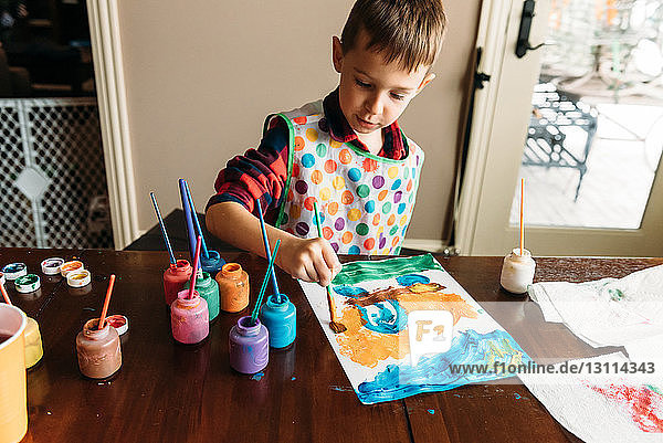 Junge malt Bild auf Papier bei Tisch im Haus