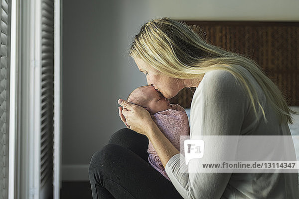 Seitenansicht einer Mutter  die ihre neugeborene Tochter küsst  während sie sie zu Hause trägt