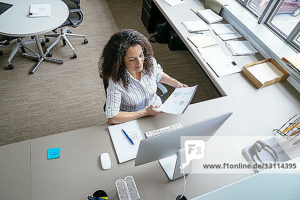 Schrägansicht einer Geschäftsfrau  die Berichte analysiert  während sie im Büro am Schreibtisch sitzt