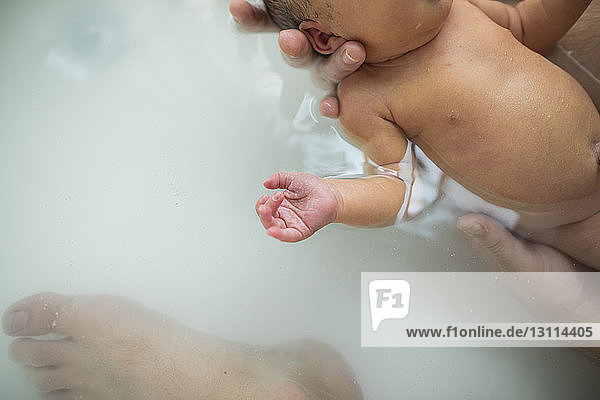 Abgehackte Hände eines Vaters  der seine neugeborene Tochter zu Hause in der Badewanne badet