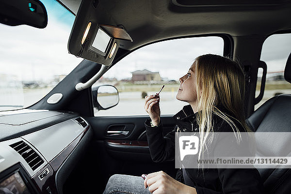 Side view of girl applying lipstick while sitting in car