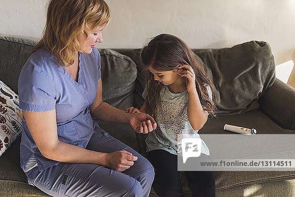 Schrägansicht eines Mädchens  das den Puls einer Ärztin kontrolliert  während sie zu Hause auf dem Sofa sitzt