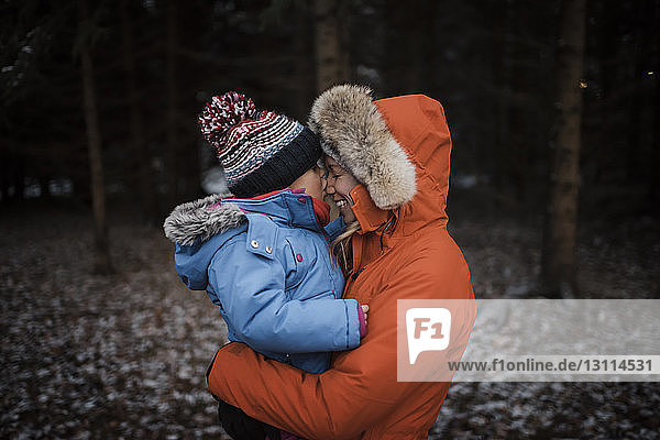 Glückliche Mutter mit Tochter im Winter im Wald stehend