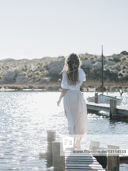 Rückansicht einer Frau  die auf einem hölzernen Pier über dem Meer vor klarem Himmel an einem sonnigen Tag steht