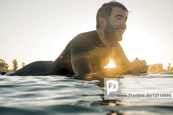 Glücklicher männlicher Surfer  der bei Sonnenuntergang auf einem Surfbrett im Meer liegt