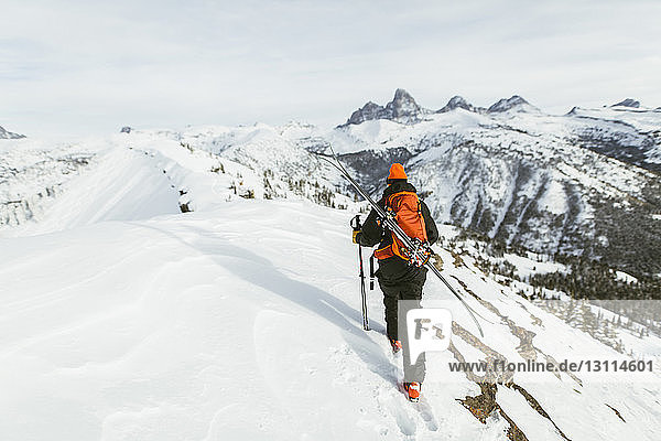 Rückansicht eines Wanderers mit Rucksack und Skistöcken beim Wandern auf einem schneebedeckten Berg