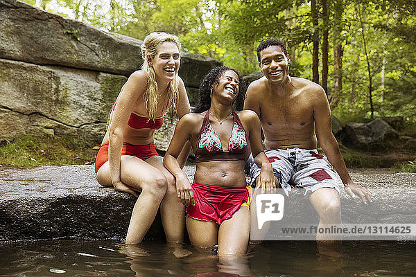 Porträt von glücklichen Freunden auf einem Felsen am Fluss sitzend