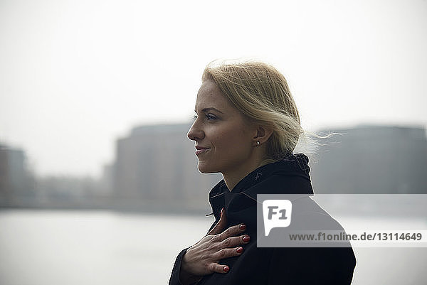 Seitenansicht einer nachdenklichen Geschäftsfrau  die weg schaut  während sie am Fluss gegen den Himmel steht