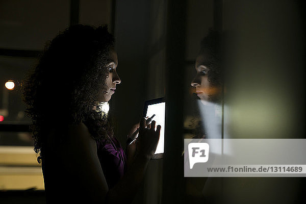 Geschäftsfrau steht am Whiteboard und benutzt Tablet-Computer in dunklem Büro