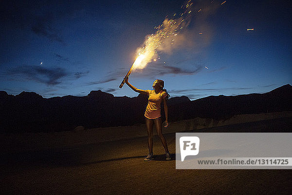 Smiling woman burning fireworks on mountain against sky at dusk