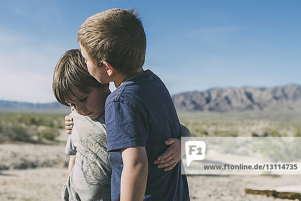 Boy kissing brother while standing at Joshua Tree National Park against sky during sunny day