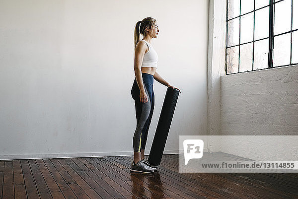 Seitenansicht einer Frau  die im Fitnessstudio stehend ein Trainingsgerät in der Hand hält