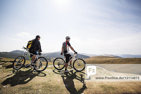 Friends standing with bicycles on mountain against sky