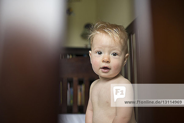 High angle view of baby boy looking through window while standing at home