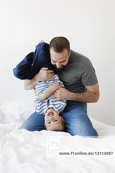Playful father carrying son upside down on bed at home