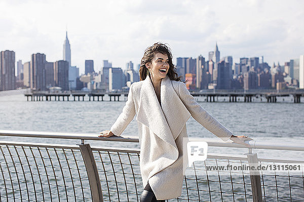 Fröhliche Frau steht auf der Promenade mit der Skyline der Stadt im Hintergrund