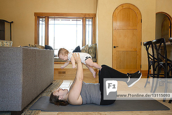 Seitenansicht einer Mutter  die einen Sohn trägt  während sie zu Hause auf einer Trainingsmatte trainiert