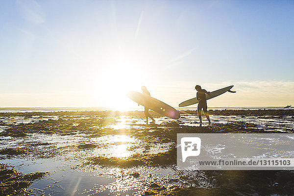 Ehepaar mit Surfbrettern beim Spaziergang am Strand des Bundesstaates San Onofre im Urlaub