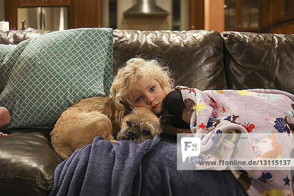 Porträt eines Mädchens mit Hund  das zu Hause auf dem Sofa liegt