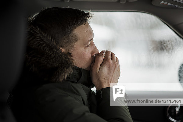 Seitenansicht eines im Auto sitzenden Mannes mit Händen auf dem Mund