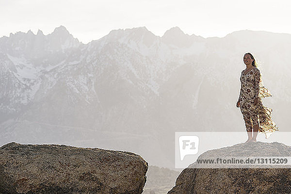 Young woman standing on rock against mountains during foggy weather