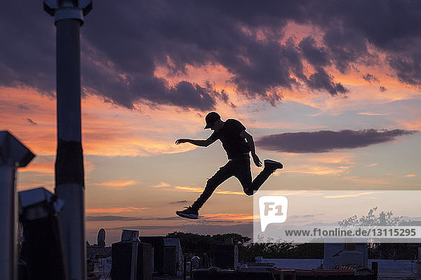 Silhouettenmann springt bei Sonnenuntergang in die Stadt