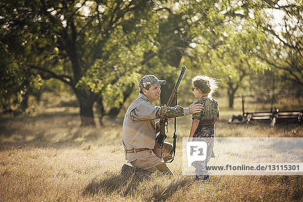 Vater mit Gewehr in der Hand  während er mit seiner Tochter auf einem Grasfeld spricht