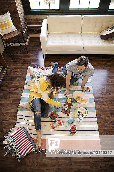 Schrägaufnahme eines Paares  das zu Hause auf einem Teppich sitzt und Essen isst