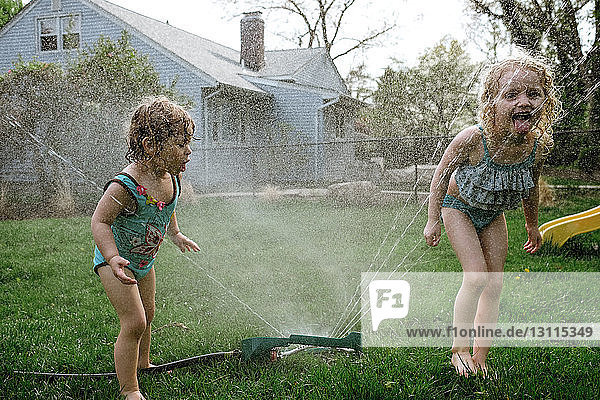 Girls drinking from spraying water at lawn