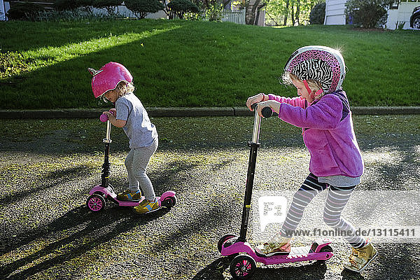 High angle view of sisters riding push scooters on road