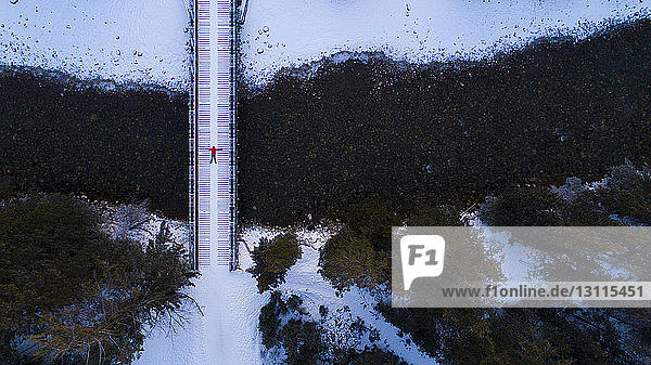 Distant view of hiker lying on footbridge in forest during winter