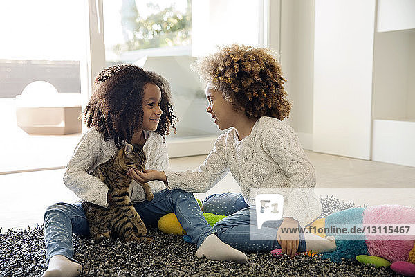 Happy sisters playing with cat at home