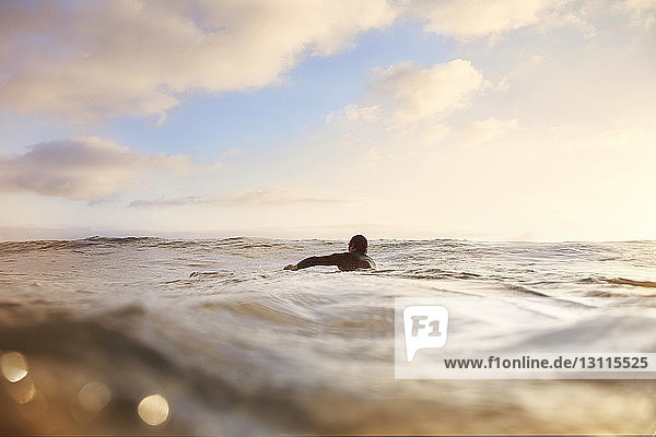 Männlicher Surfer  der im Meer gegen den Himmel schwimmt