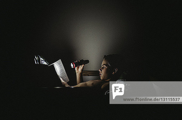 Junge hält Taschenlampe  während er zu Hause ein Buch liest